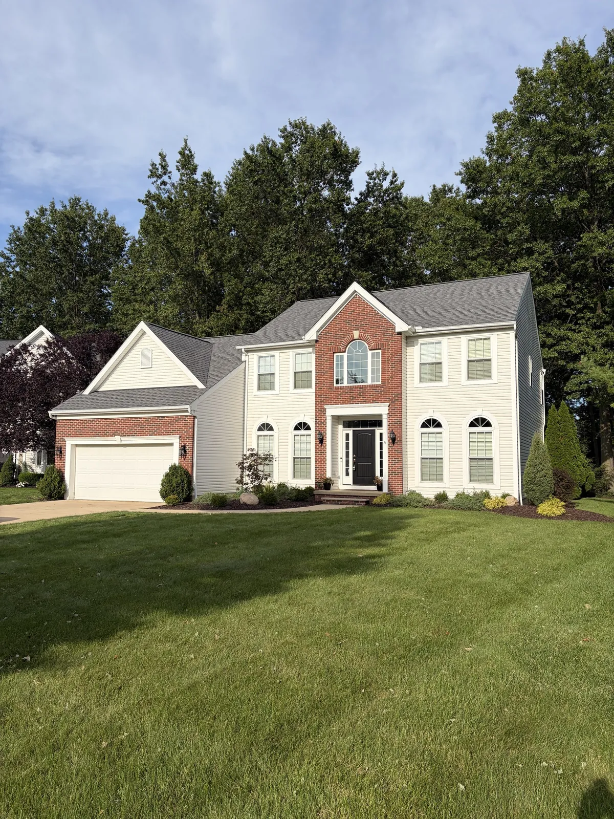 Street view of a two-story home with a brick and cream siding front and a large lawn in Avon Lake, Ohio after an Atlas shingle roof replacement