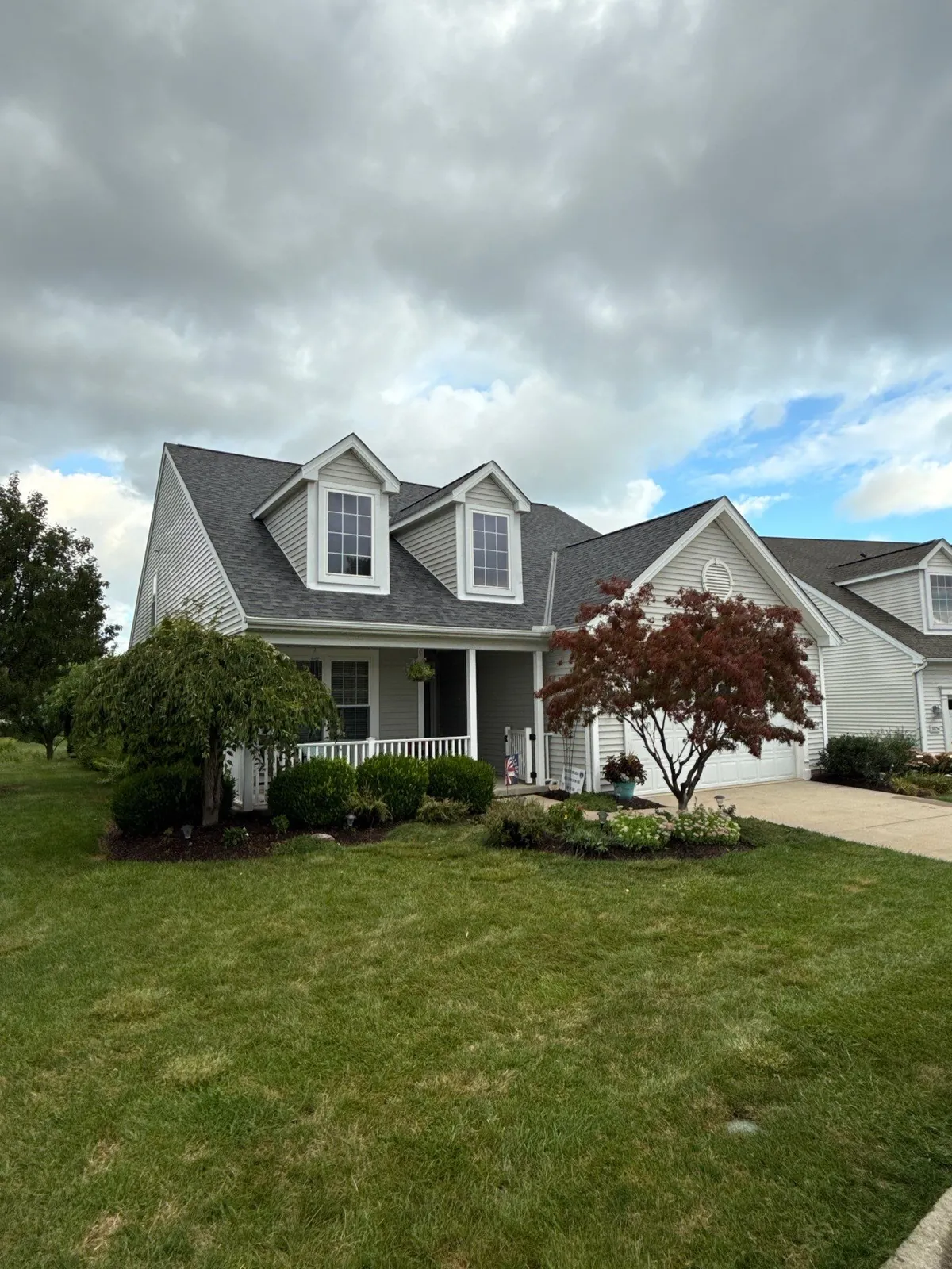 Gray-sided home with two front dormers, a covered porch, and a new shingle roof behind a red Japanese maple in Avon Lake, Ohio