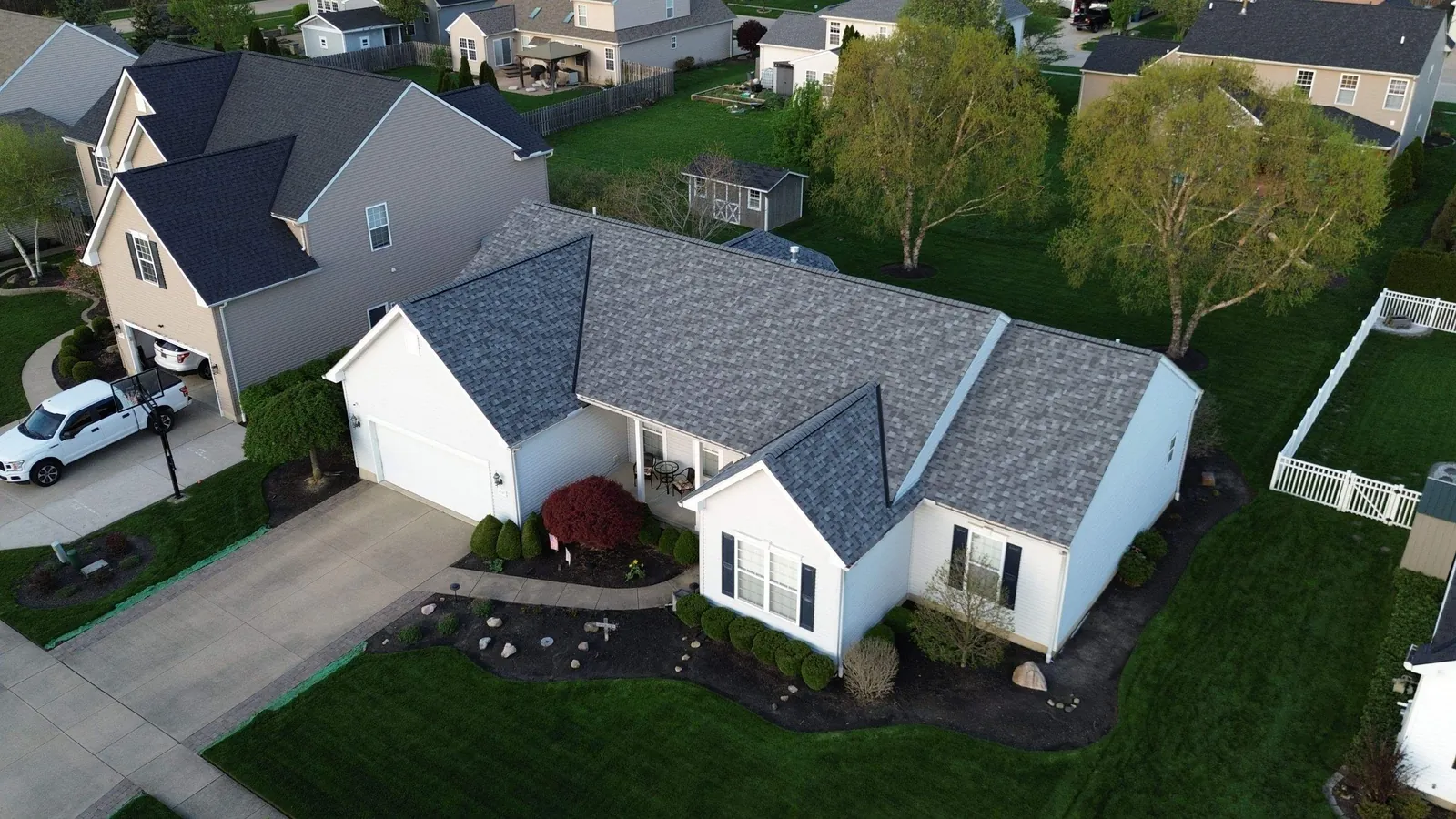 Drone view of a white single-story home with gray architectural shingles, an attached garage, and landscaped beds in an Avon, Ohio neighborhood