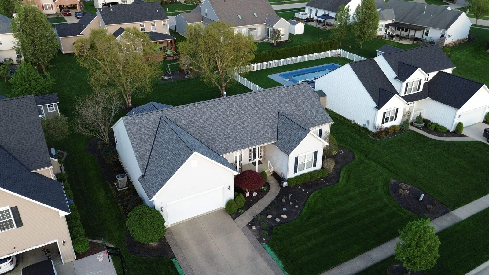 Aerial view of the same white Avon, Ohio home from the side, showing the full gray shingle roof, driveway, and neighboring backyard pool
