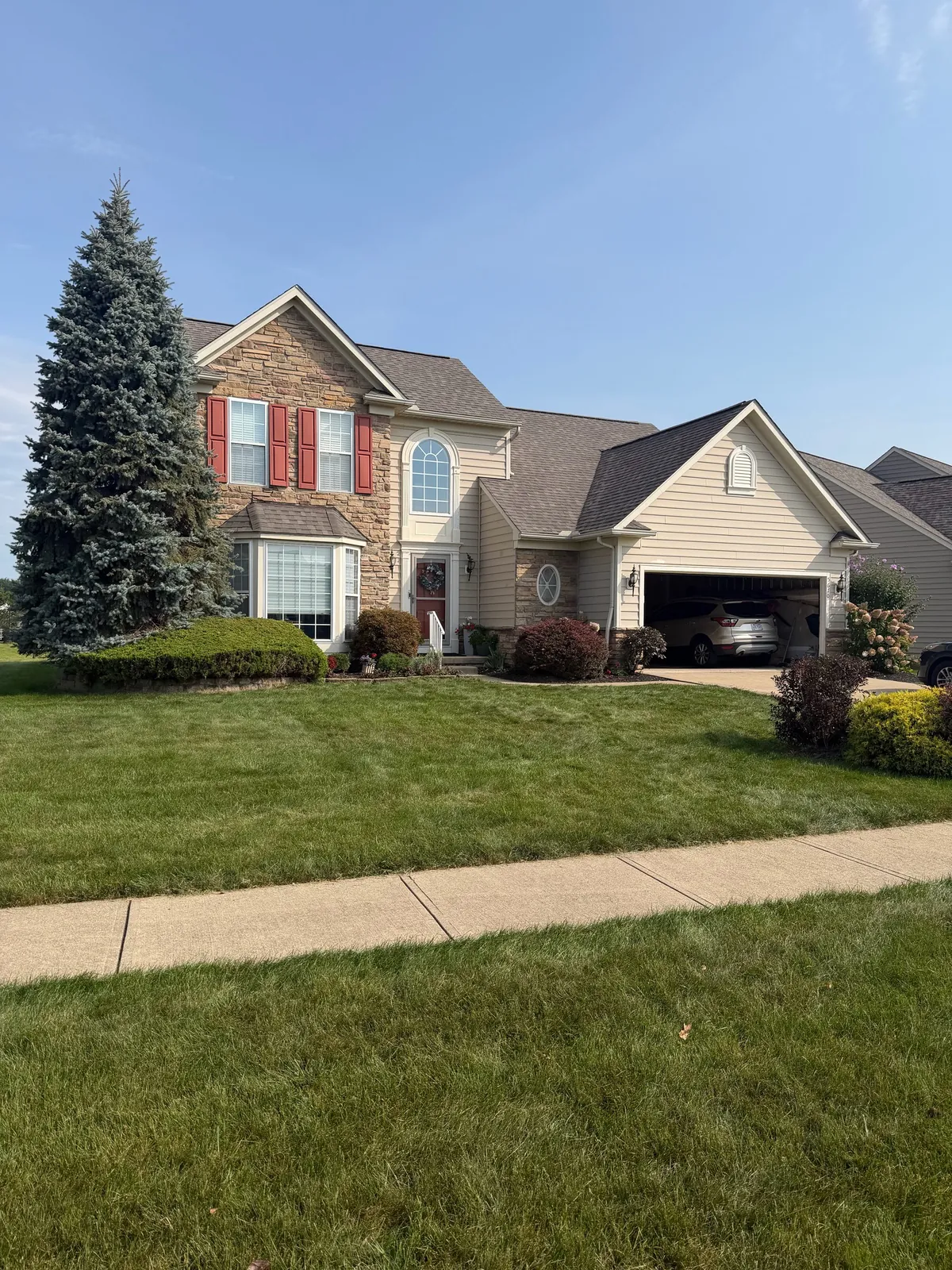 Street view of a two-story home with a stone front, tan siding, and red shutters in Avon, Ohio, with a new Owens Corning Duration Onyx Black roof