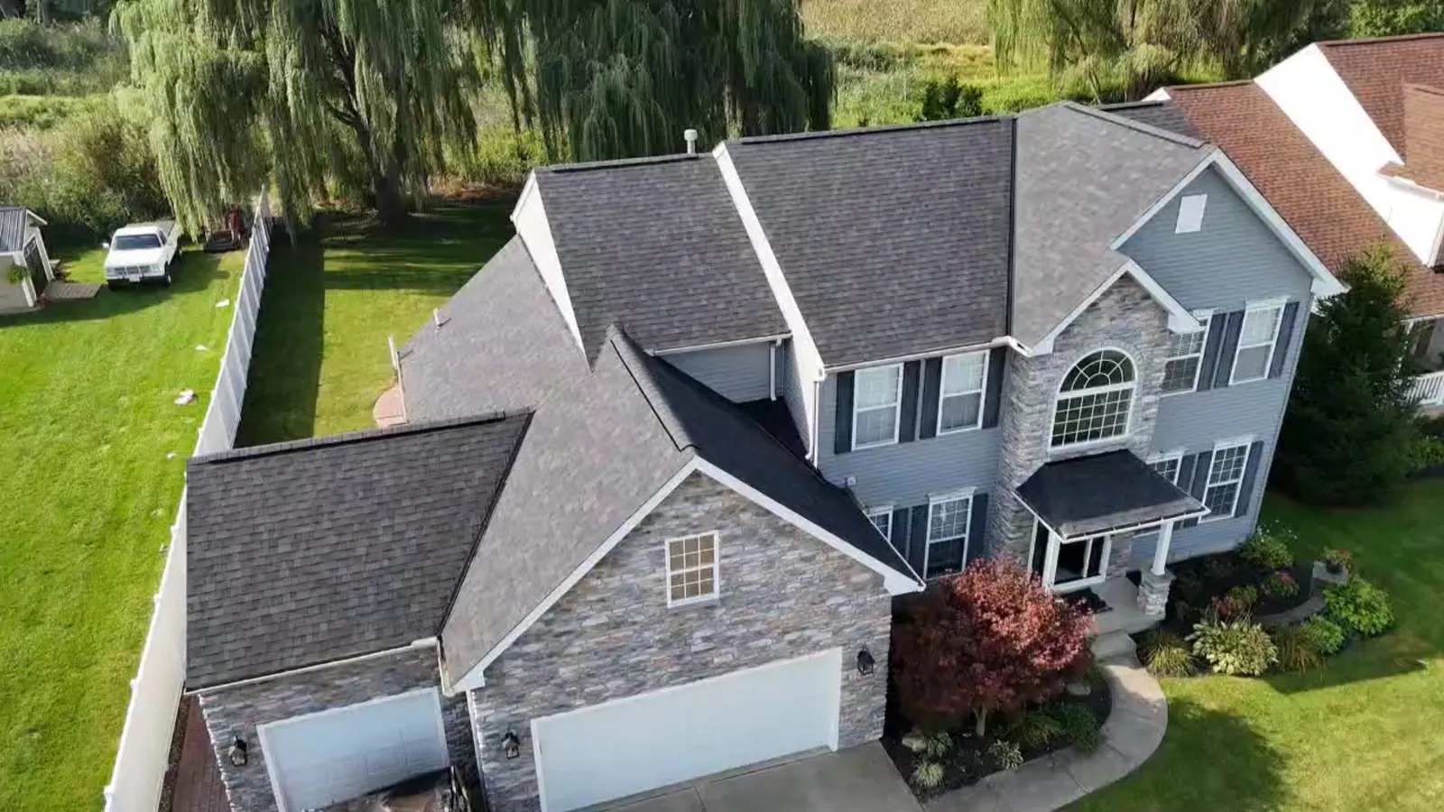 Aerial view of a two-story home with grey-blue siding and stone veneer in Avon, Ohio, with a new Owens Corning Duration Onyx Black roof
