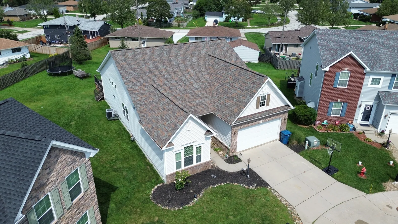 Aerial view of a white-sided home with an attached garage in Bedford, Ohio, with a new Owens Corning Duration Aged Copper roof, next to neighboring brick homes
