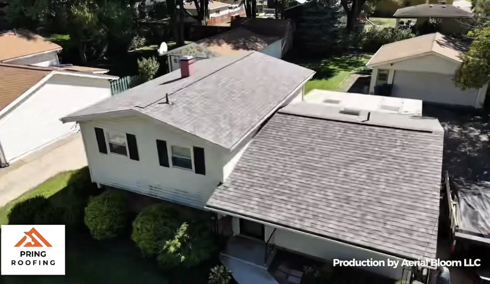 Aerial view of a two-level white-sided home with black shutters and a brick chimney in Berea, Ohio, showing both roof sections finished in Owens Corning Driftwood shingles