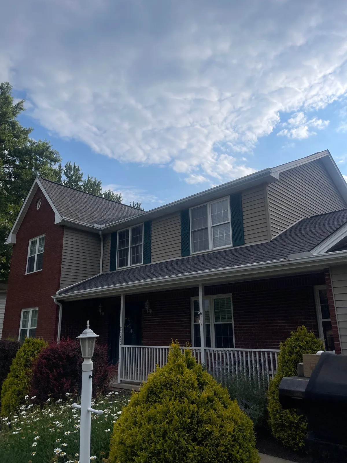 Brick and tan-sided two-story home with green shutters, a covered front porch, and a new gray shingle roof in Broadview Heights, Ohio