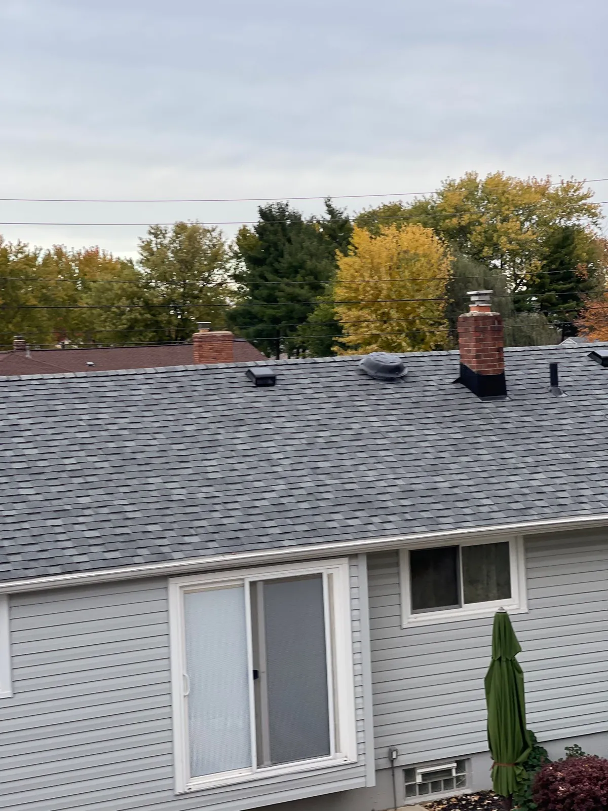 New gray shingle roof with a brick chimney above light siding on a home in Brook Park, Ohio