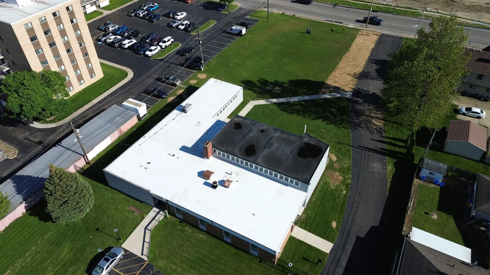 Aerial view of a low commercial building in Cleveland, Ohio with a new white Carlisle TPO roof, next to a parking lot and a multi-story office building