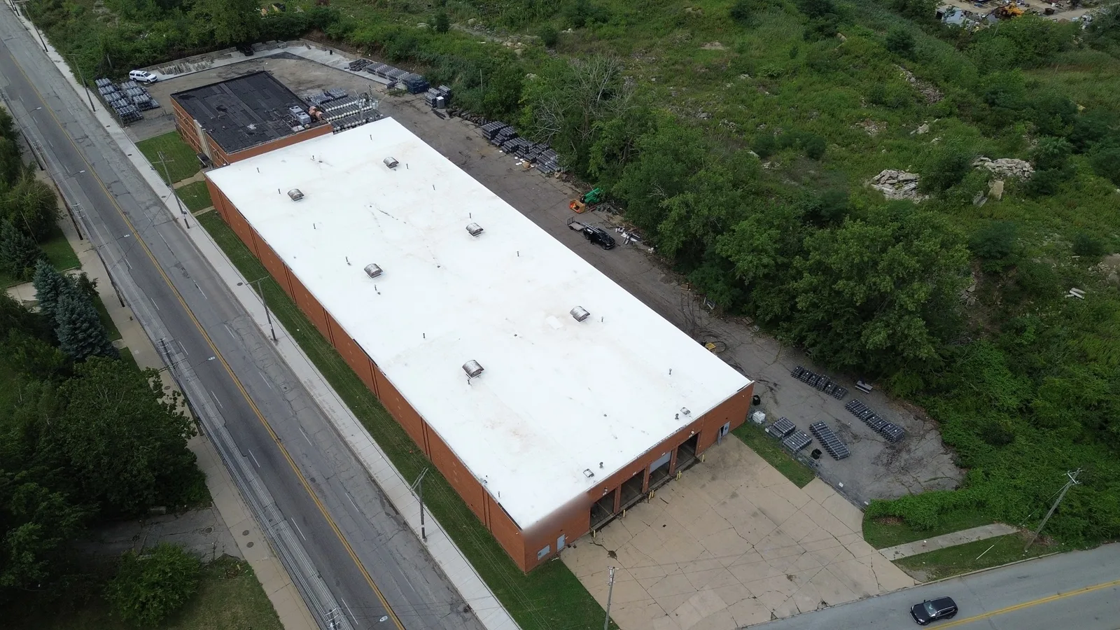 Drone view of a long one-story brick warehouse in Cleveland, Ohio, with a new white 60 mil Carlisle TPO roof, rooftop vents and hatches, loading docks and a concrete apron at the near end.