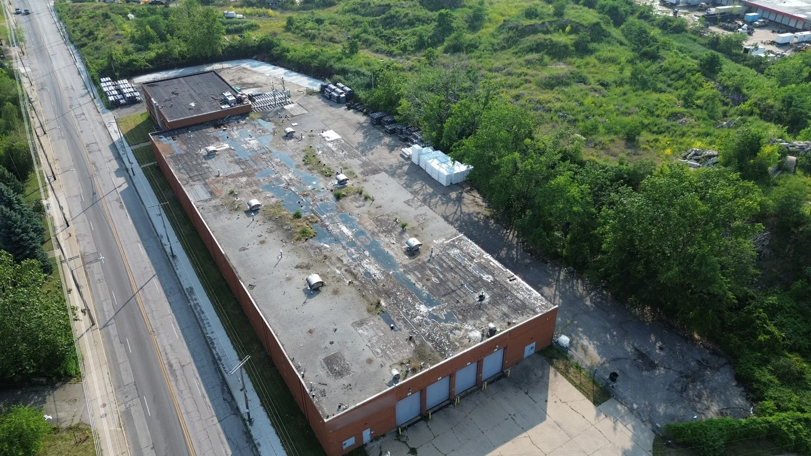 Drone view of the old, neglected flat roof on a long one-story brick warehouse in Cleveland, Ohio, with ponding water across the surface before tear-off.
