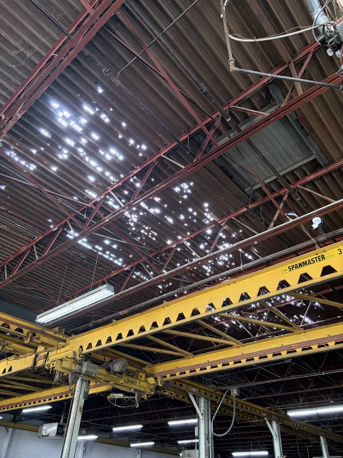 Holes in the rusted steel roof deck above the overhead crane inside a Cleveland warehouse, exposed during tear-off.