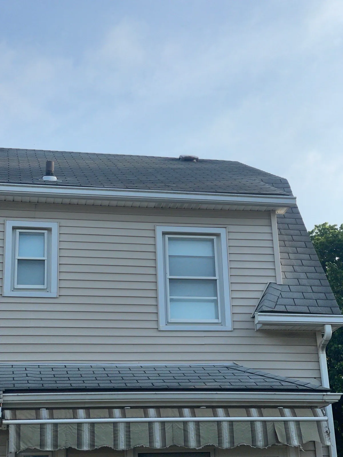 Side of a tan-sided home in Cleveland's Kamm's Corners neighborhood showing the new shingle roof and lower porch roof