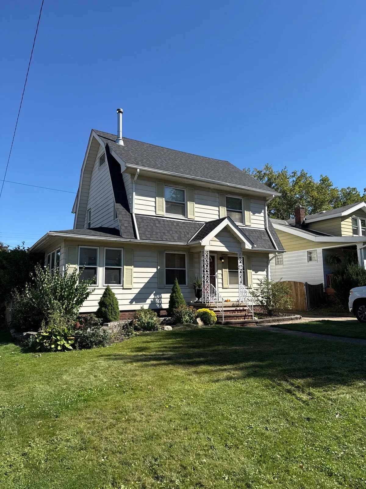 Cream two-story home with a covered front porch and a new gray shingle roof on a sunny day in Cleveland, Ohio