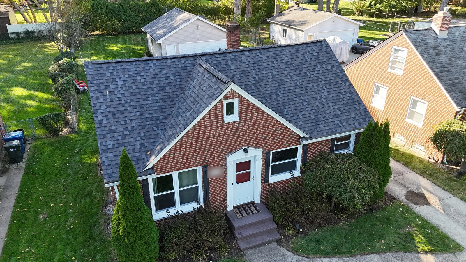 Drone view of a red brick Cape Cod bungalow in Fairview Park, Ohio, with a new Owens Corning Duration roof in Williamsburg Gray, white trim, dark shutters, and a front gable over a white entry door.