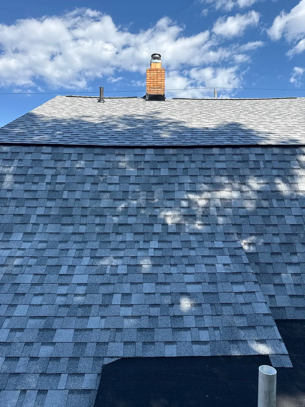 Rooftop view of new gray architectural shingles and a brick chimney on a Lakewood, Ohio home