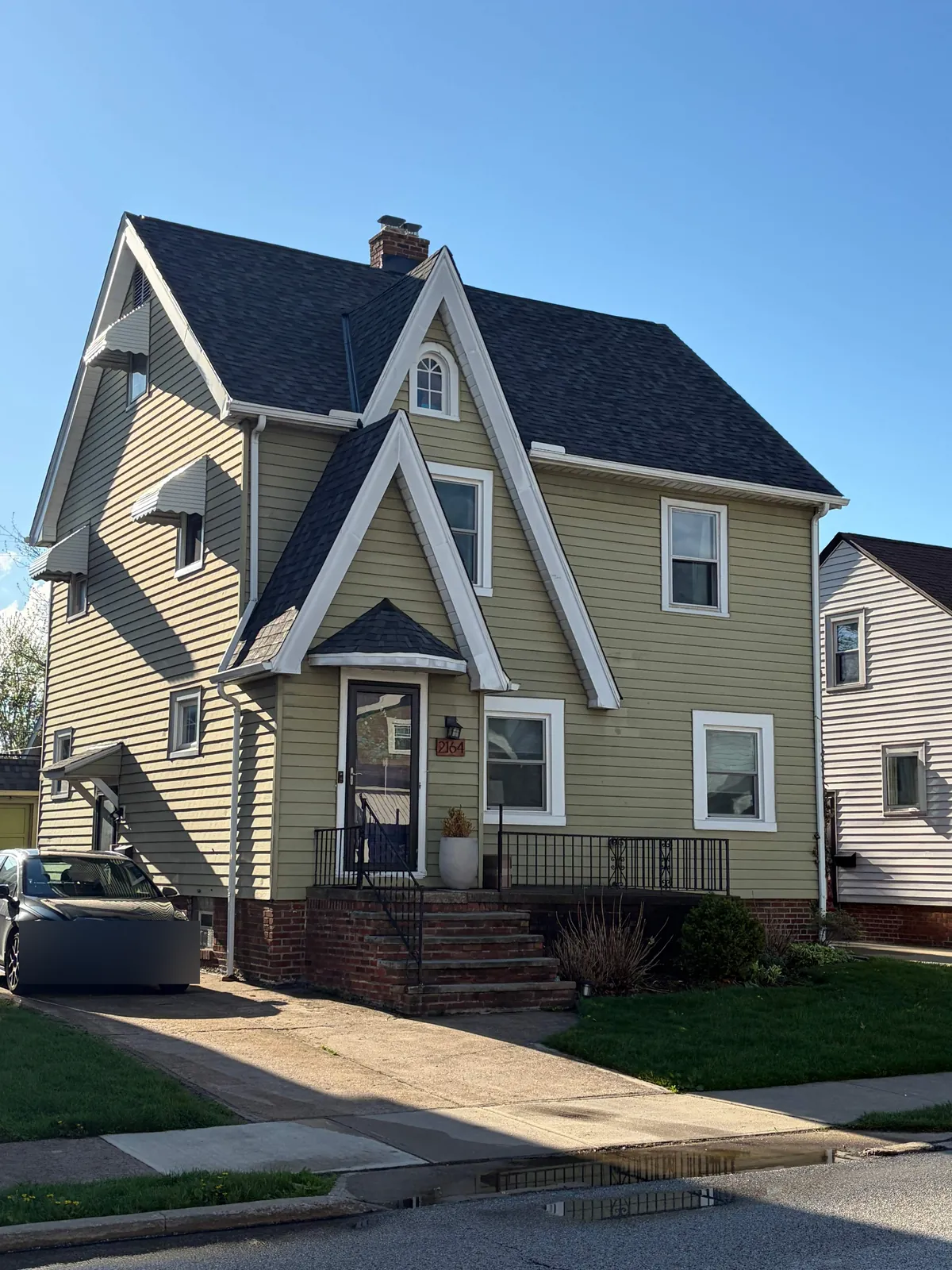 Street view of a steep-gabled green two-story home with white trim and a dark shingle roof in Lakewood, Ohio
