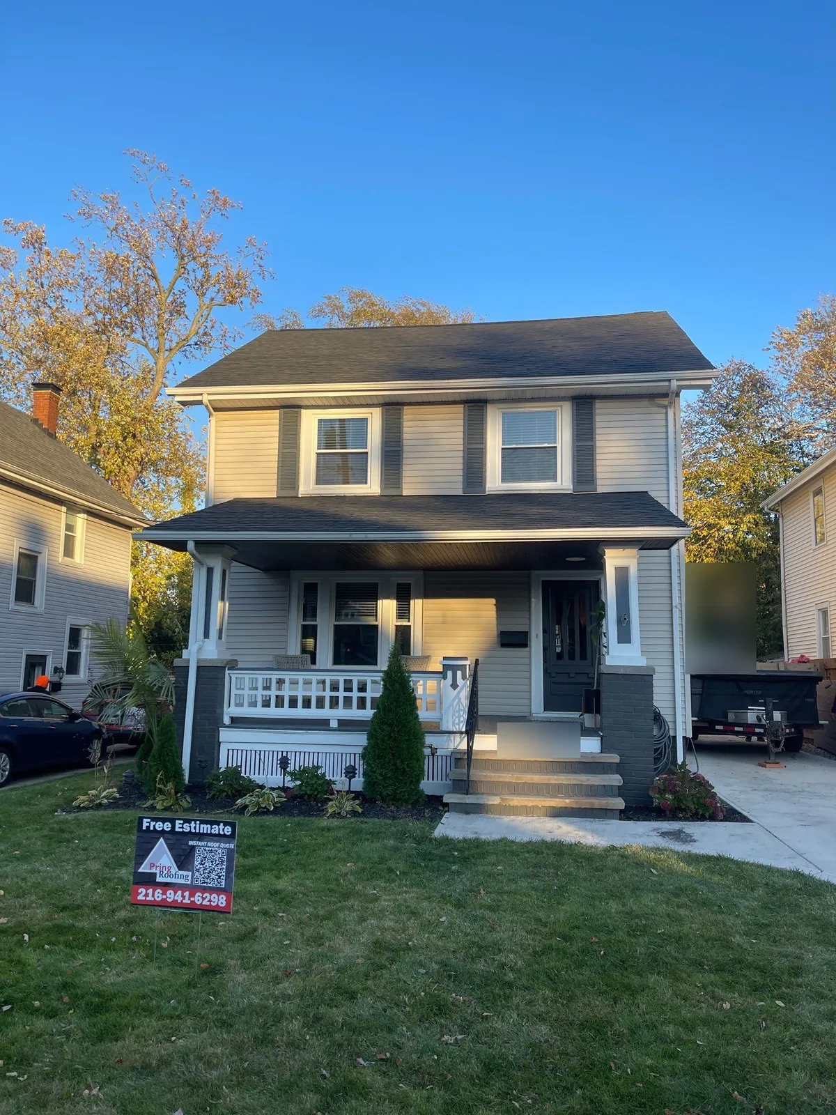 Gray two-story Lakewood, Ohio home with a covered front porch and a new dark shingle roof behind a Pring Roofing yard sign