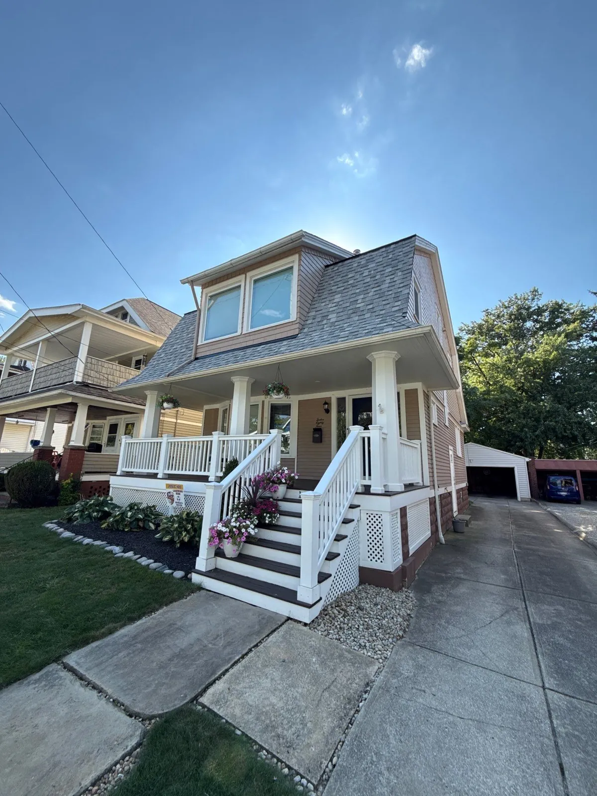 Tan two-story Lakewood, Ohio home with a white front porch, flower-lined steps, and a new gray shingle roof