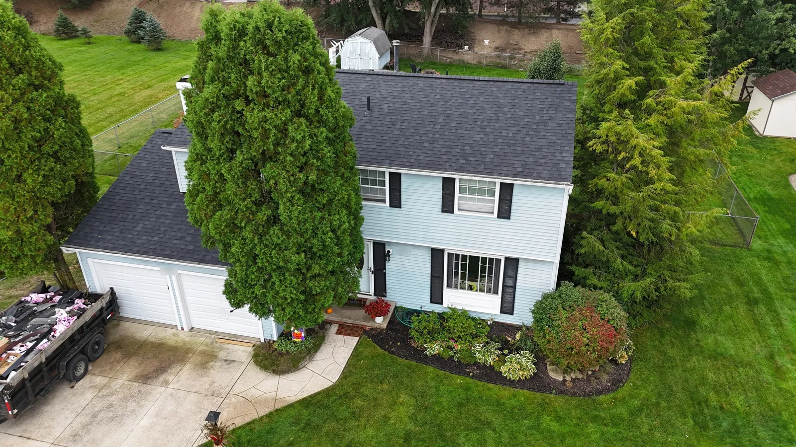 Drone view of a two-story colonial in Macedonia, OH with light blue siding, black shutters, and a new Owens Corning Duration Onyx Black shingle roof over the house and attached garage