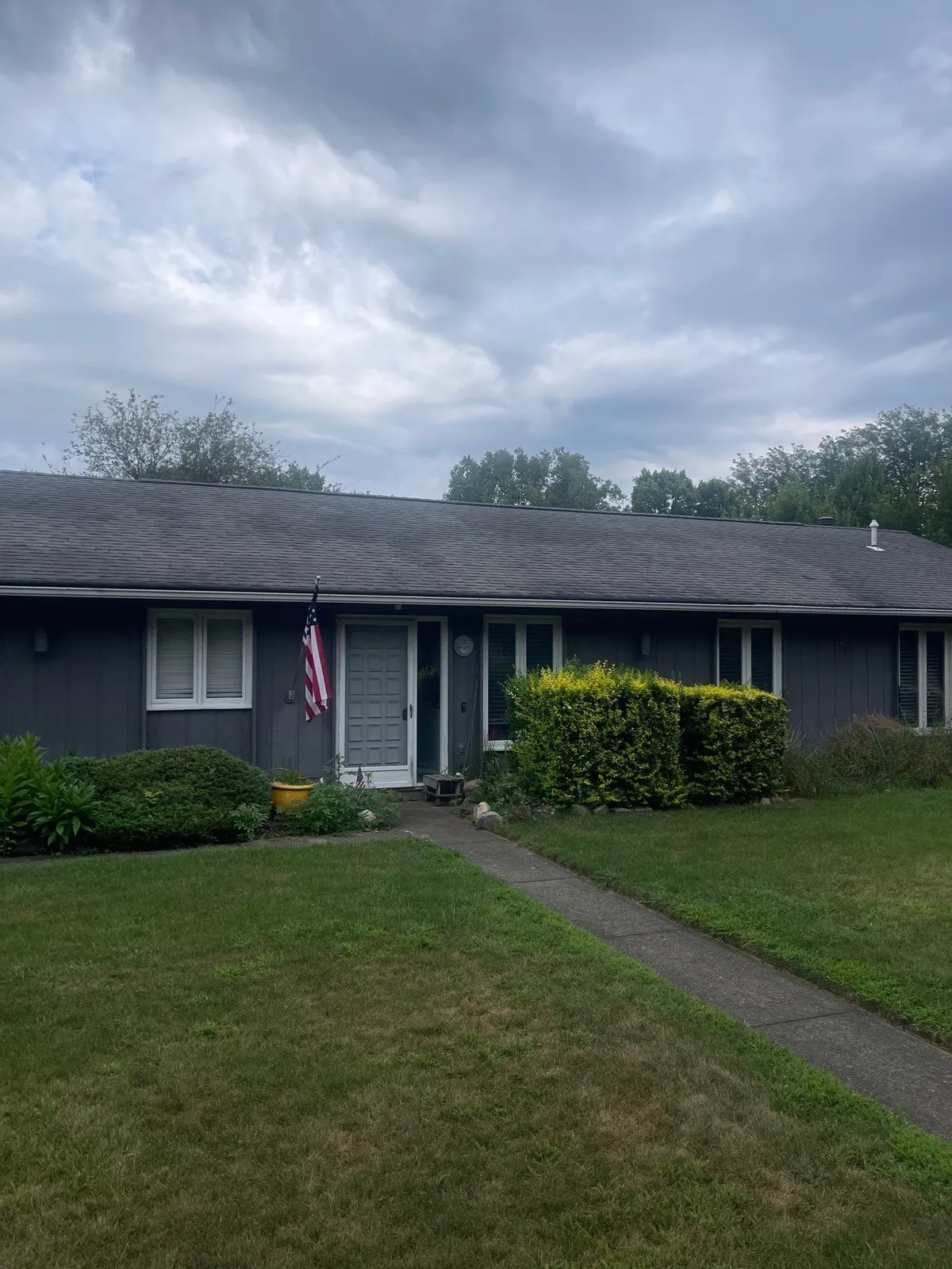 Long ranch home with dark siding, new gray shingles, and new gutters under a cloudy sky in Medina, Ohio