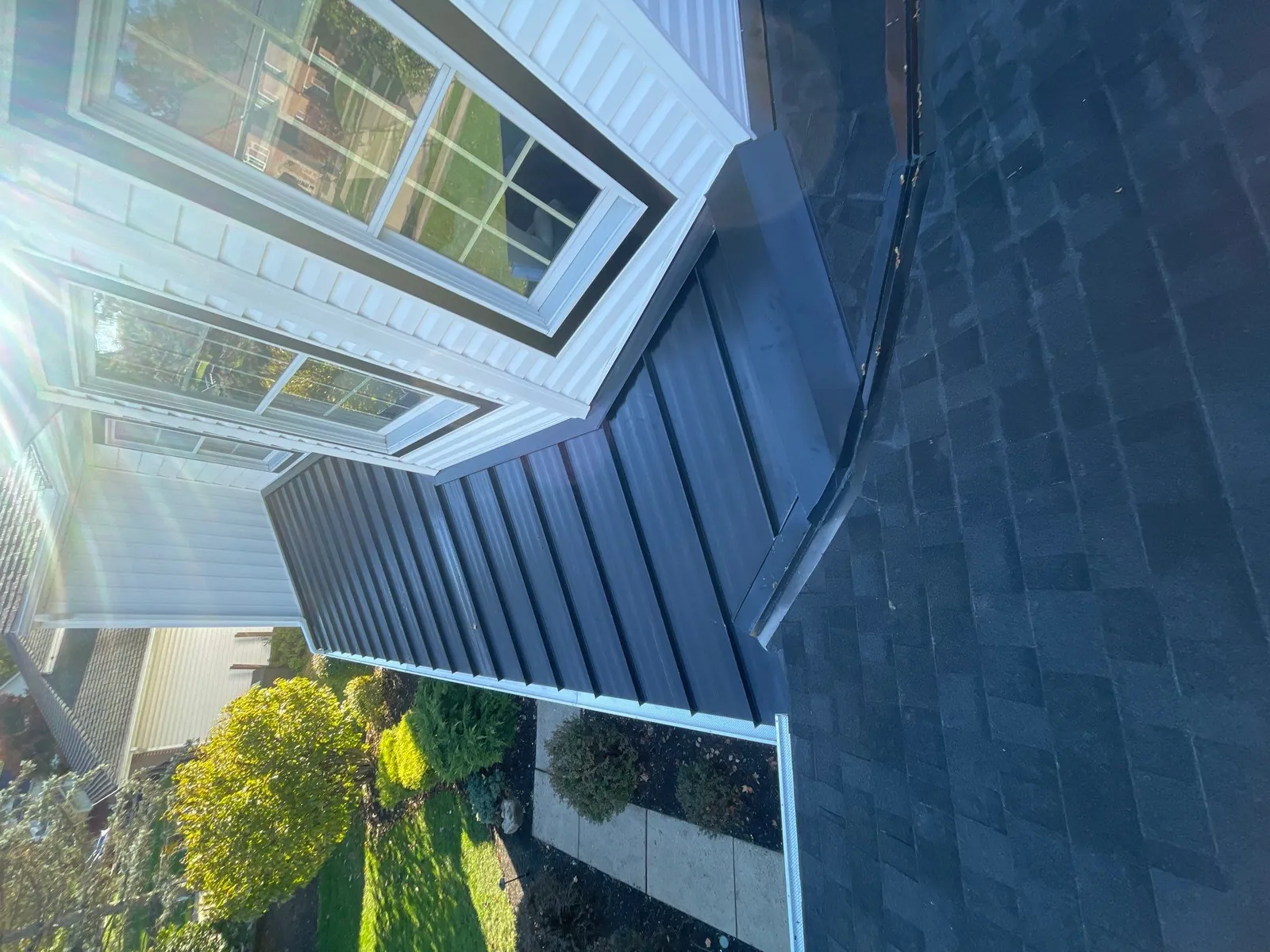 Close-up from above of a new dark standing seam metal roof section meeting Owens Corning shingles and white siding in Munroe Falls, Ohio