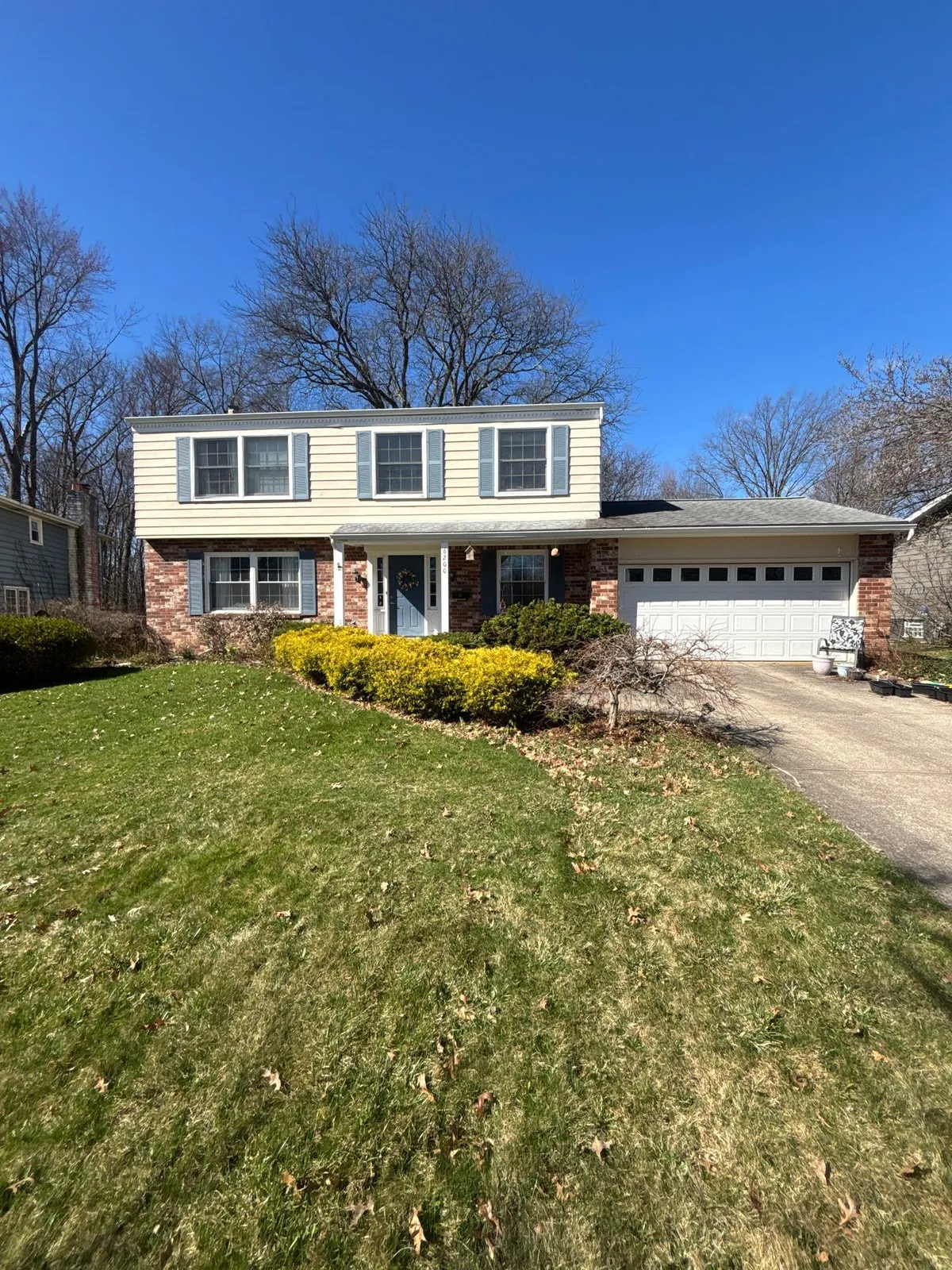 Two-story home with cream siding, a brick lower level, and a gray shingle roof on a sunny spring day in North Olmsted, Ohio