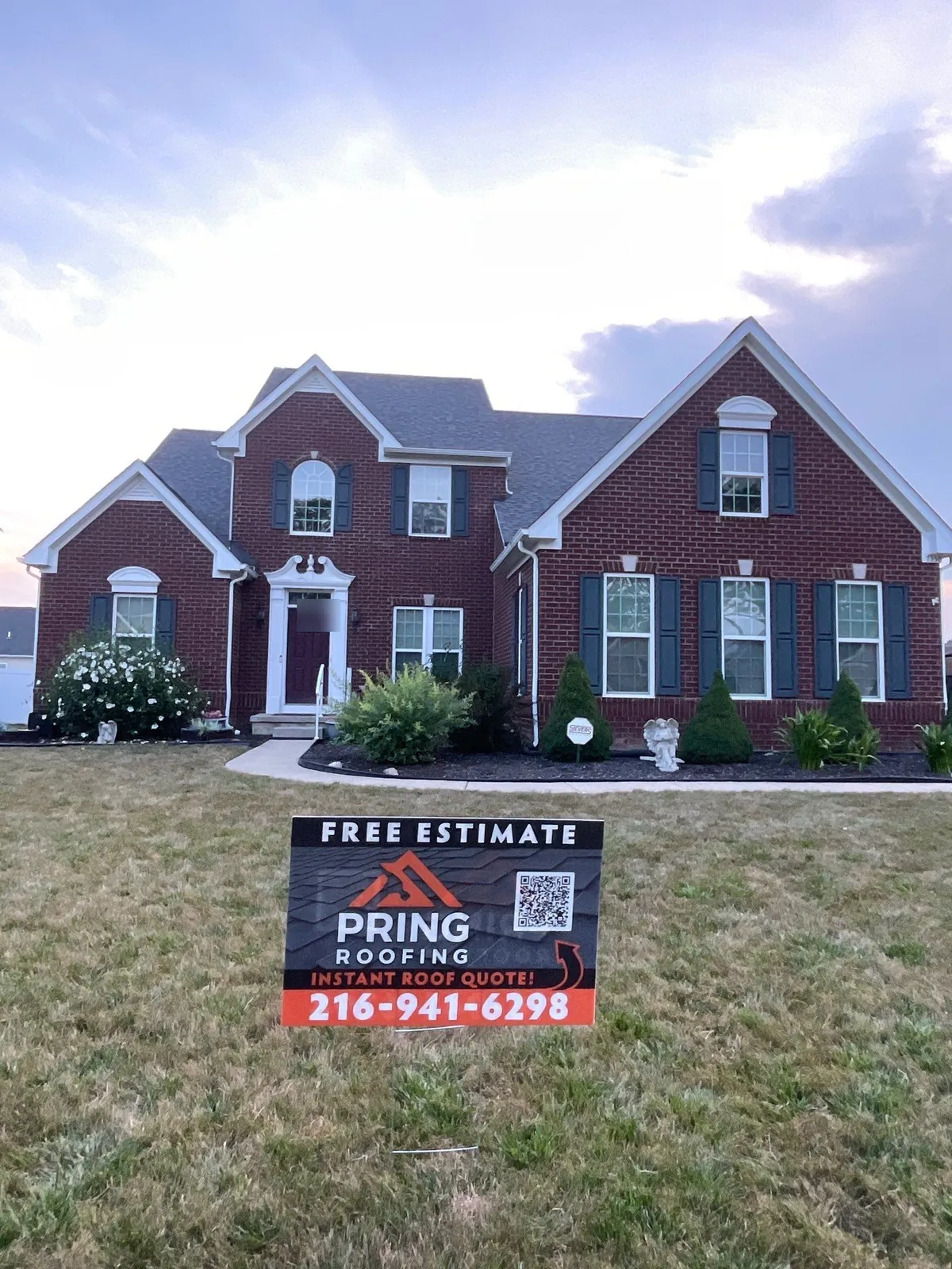 Red brick two-story colonial with dark shutters and a new gray shingle roof behind a Pring Roofing yard sign in North Ridgeville, Ohio