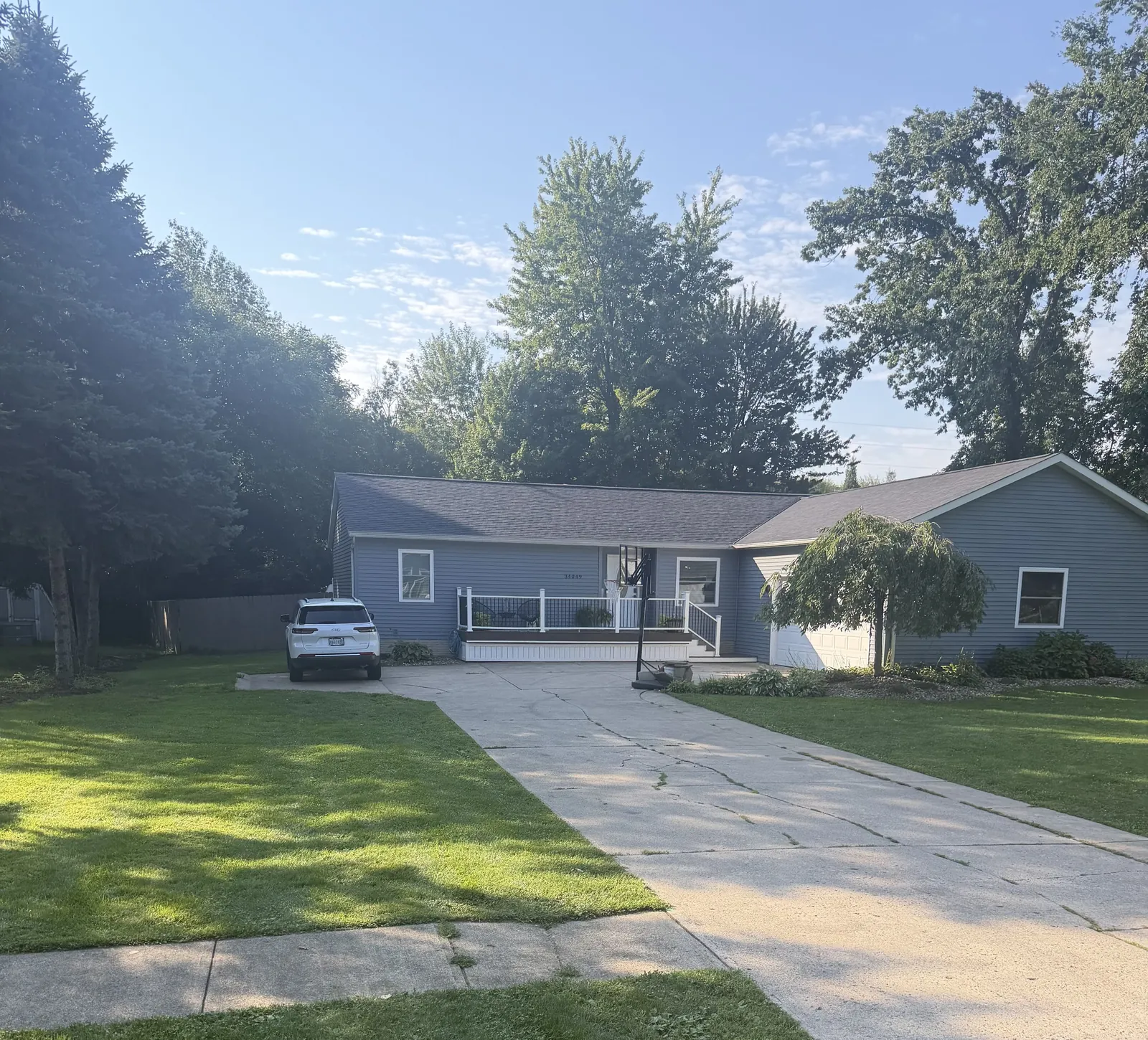 Ranch home with light blue-gray siding, a white porch railing, and a long concrete driveway in North Ridgeville, Ohio, with a new Owens Corning Duration Onyx Black roof
