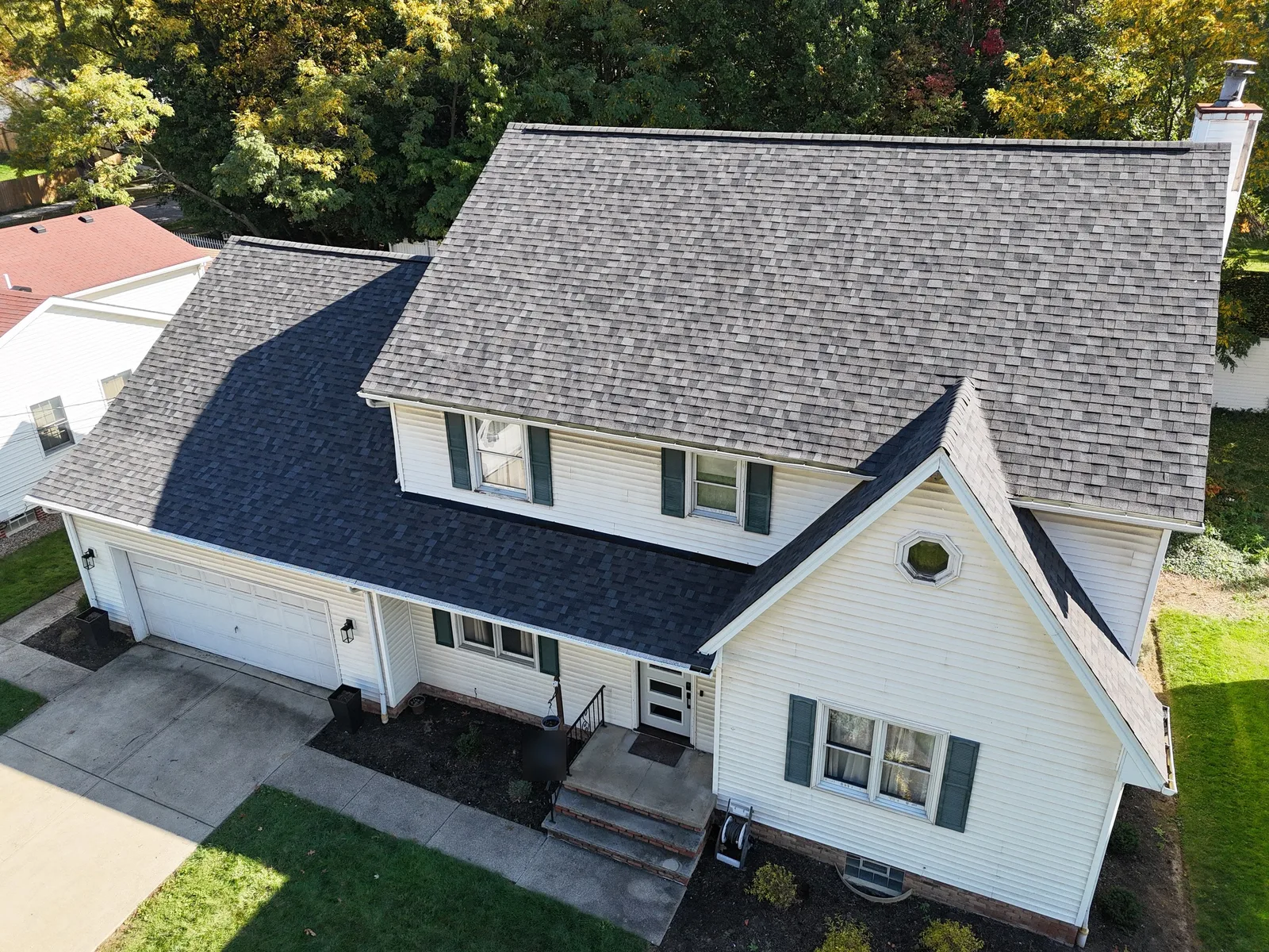 Drone view of a two-story colonial in Parma, Ohio, with white vinyl siding, dark green shutters, and a new Owens Corning Duration roof in Williamsburg Gray over the main house, garage, and front entry.