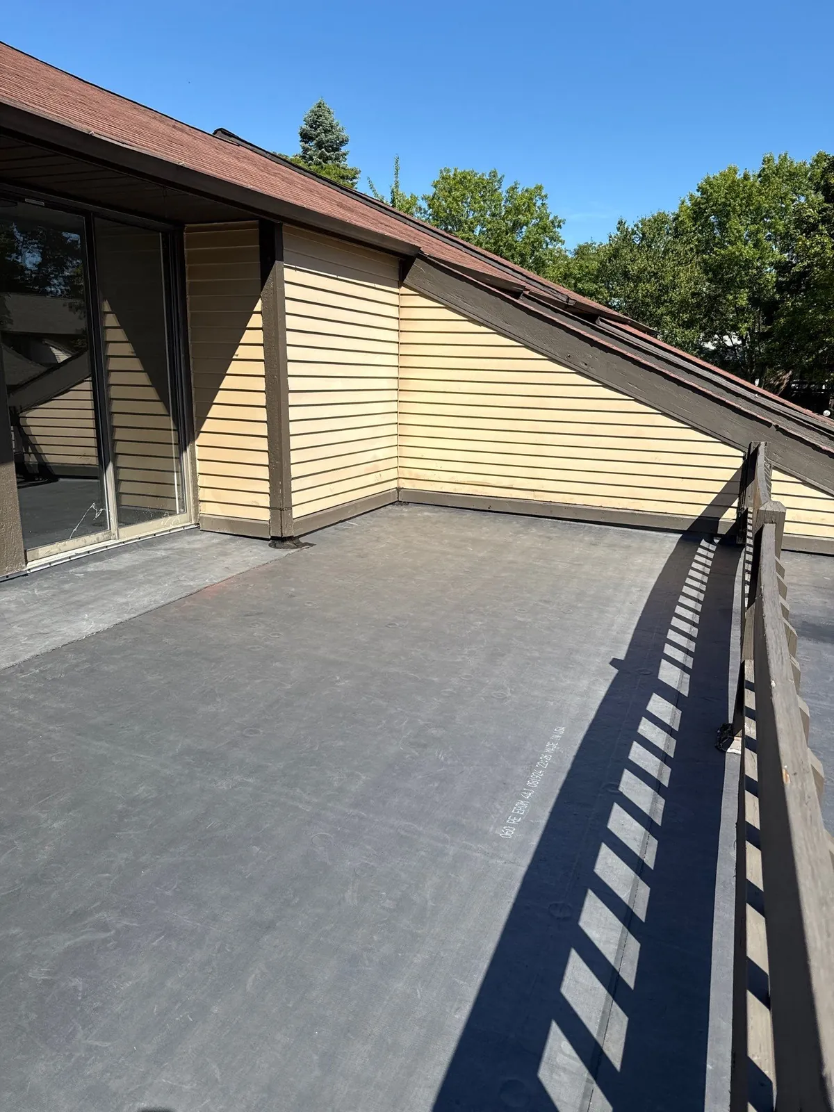 New dark EPDM rubber membrane on a flat townhome roof deck beside yellow siding in Richmond Heights, Ohio
