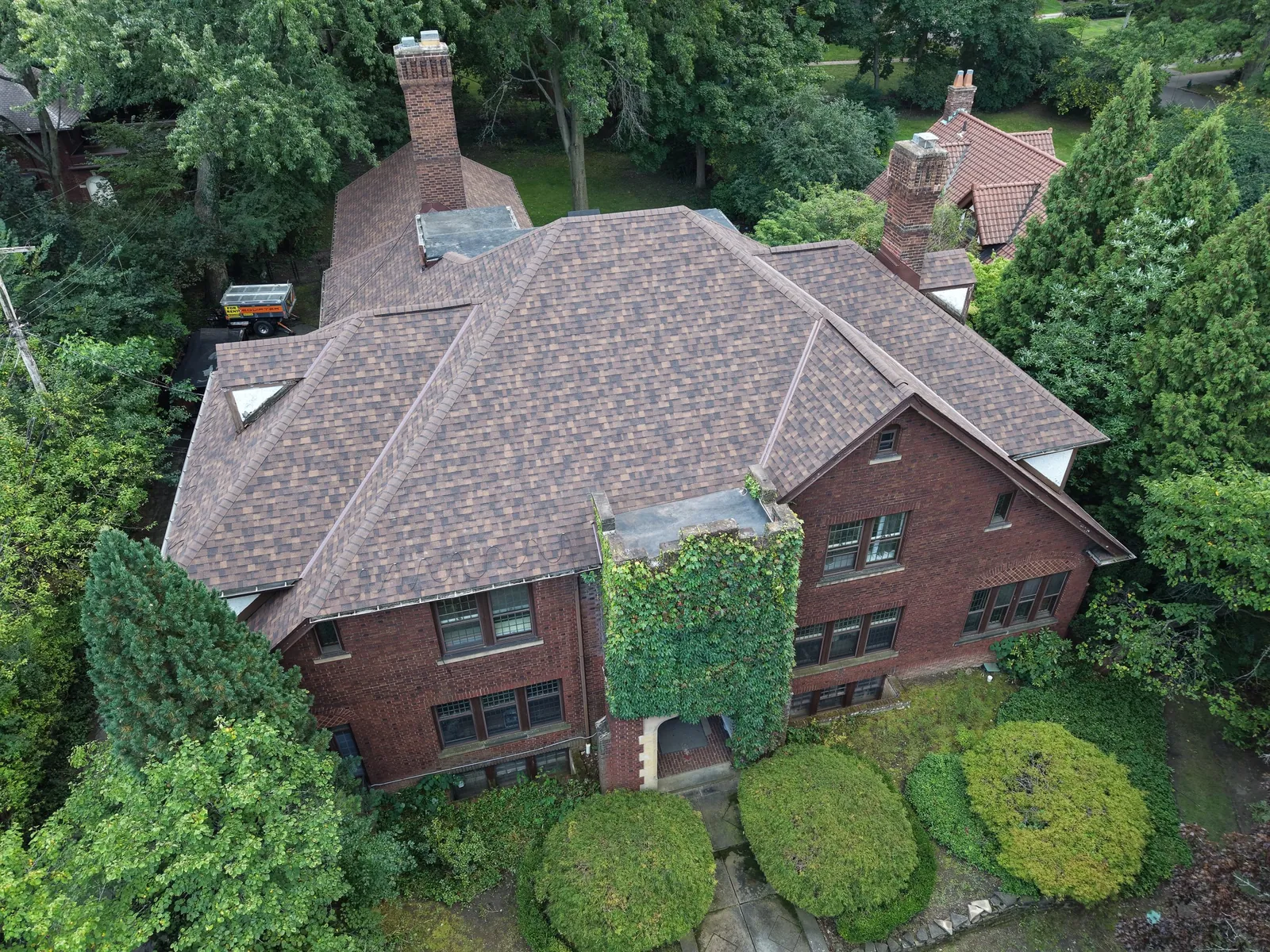 Aerial view of a large brick home with two chimneys and an ivy-covered stone entry in Shaker Heights, Ohio, with a new Owens Corning Duration Brownwood roof