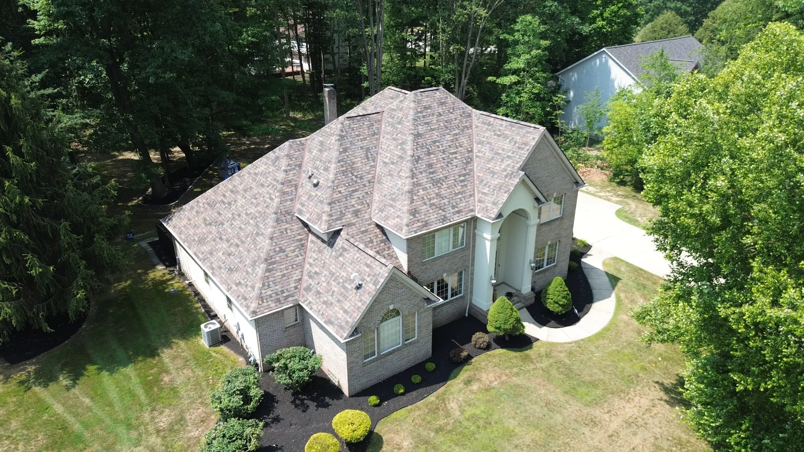 Aerial view of a large tan two-story home in Solon, Ohio with a new Owens Corning TruDefinition Duration FLEX roof in Summer Harvest, multiple gables, and landscaped front beds