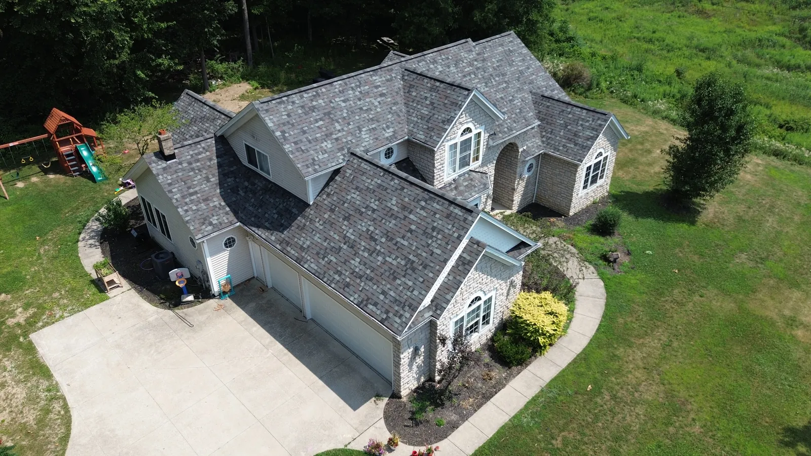 Drone photo of a gray-sided two-story home with stone accents and a three-car garage in Solon, Ohio, with a new Owens Corning TruDefinition Storm Cloud shingle roof