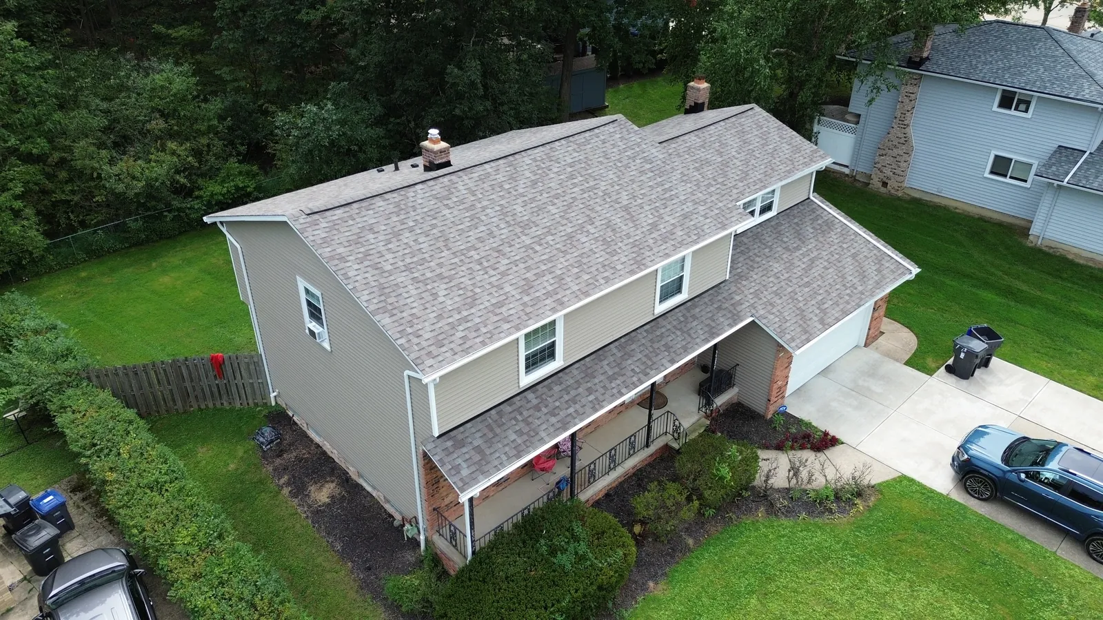 Aerial view of a two-story home in Solon, Ohio with a new Owens Corning Duration Driftwood roof, new tan siding, white gutters, and a covered front porch after hail damage