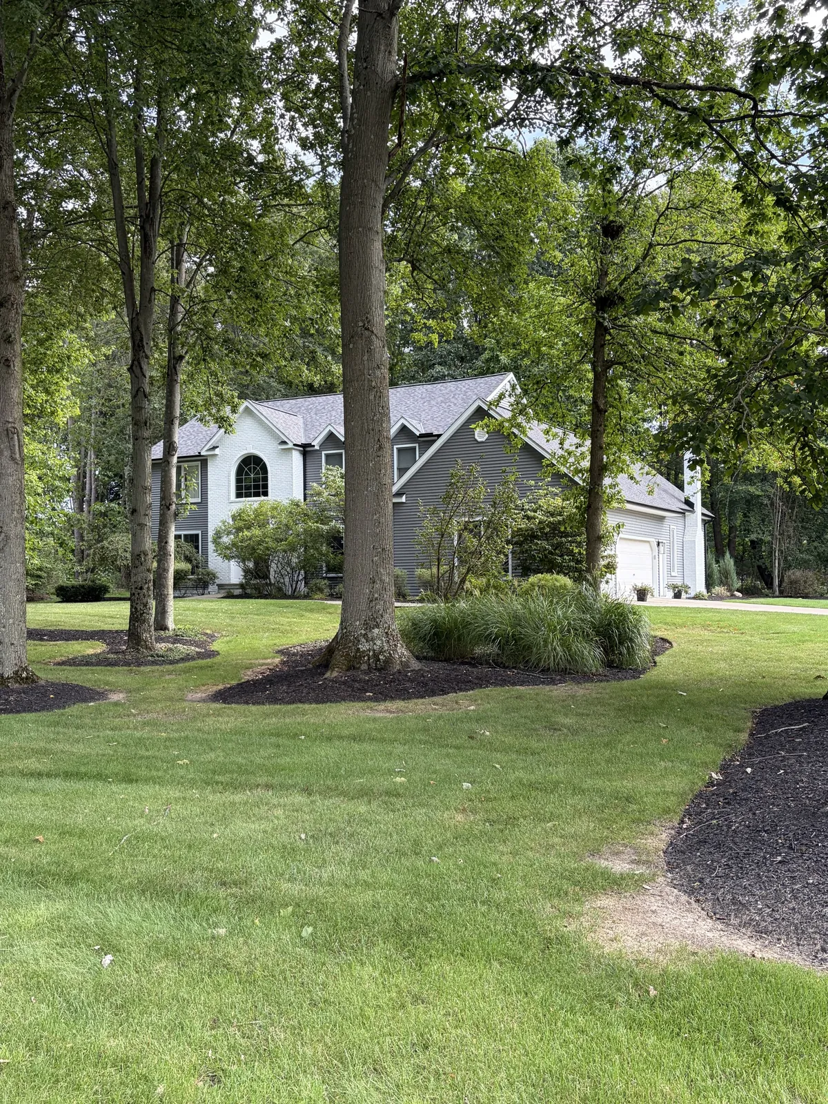 Two-story Solon, OH home with new white and gray two-tone siding and an Owens Corning Duration Williamsburg Gray roof, framed by tall trees on a wide lawn