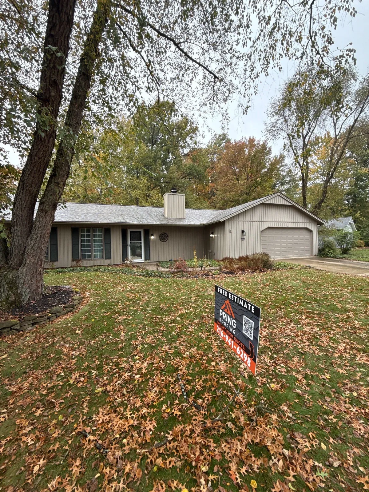Ranch home with tan siding and a new shingle roof behind a tree and fall leaves in Strongsville, Ohio