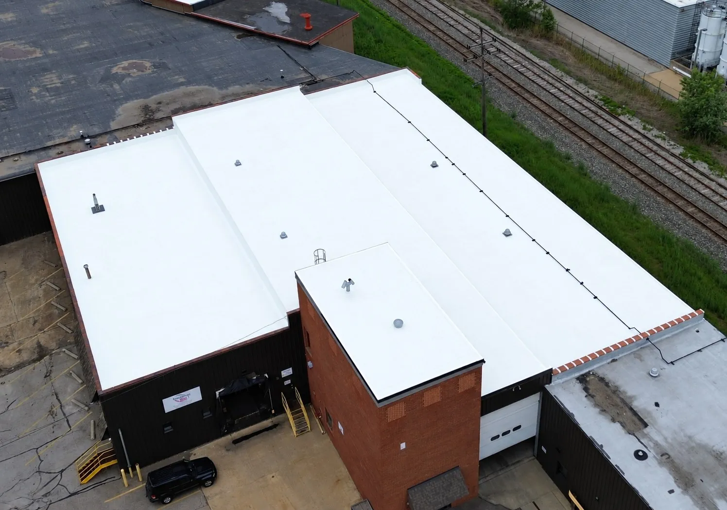 Aerial view of a multi-level industrial building beside railroad tracks in Wickliffe, Ohio with a new white Carlisle TPO roof on each tier